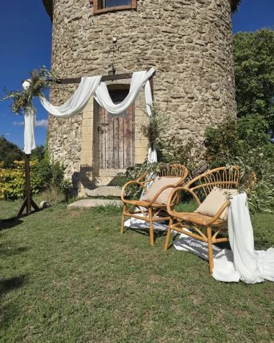 décoration de mariage provençal devant une batisse en pierre, chaises en rotin et arche décorée